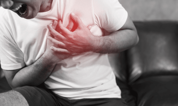 Man with a pained expression clutching his chest with his hands, representing chest pain
